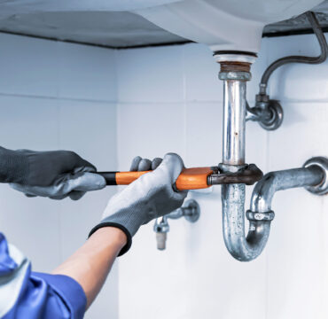 Technician plumber using a wrench to repair a water pipe under the sink. Concept of maintenance, fix water plumbing leaks, replace the kitchen sink drain, cleaning clogged pipes is dirty or rusty.